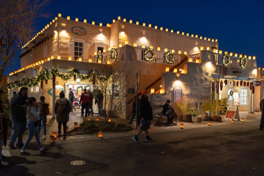 2024 OTHS- 4 People walking around at night outside of an Old Town shop that is decorated for Christmas.